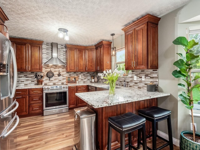kitchen featuring appliances with stainless steel finishes, a wealth of natural light, wall chimney range hood, and a peninsula