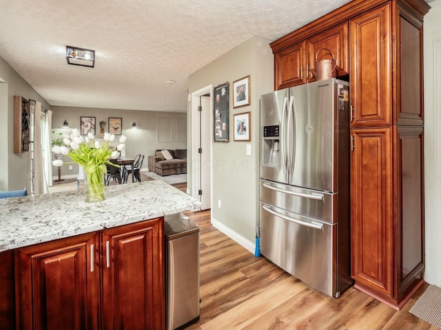 kitchen with light stone counters, stainless steel fridge, a textured ceiling, light wood finished floors, and open floor plan