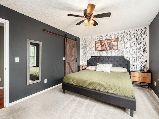 bedroom featuring an accent wall, a barn door, carpet, and baseboards