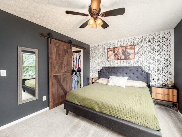 bedroom with carpet flooring, a barn door, baseboards, a textured ceiling, and an accent wall