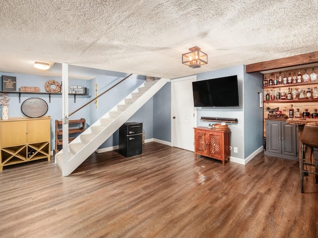 living room featuring wood finished floors, stairs, baseboards, a textured ceiling, and a dry bar