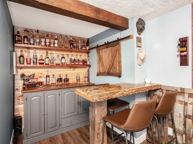 bar featuring a textured ceiling, a barn door, a dry bar, beam ceiling, and wood finished floors
