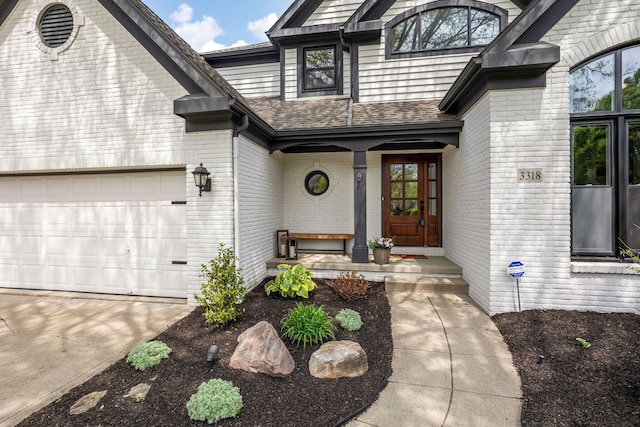 property entrance with an attached garage, a shingled roof, concrete driveway, and brick siding