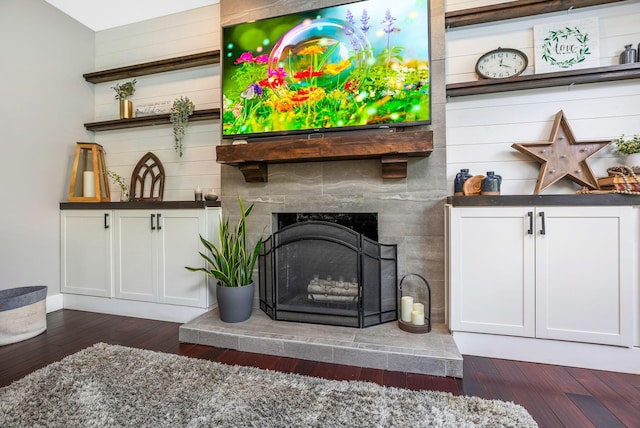 living area featuring dark wood-style flooring, baseboards, and a fireplace with raised hearth