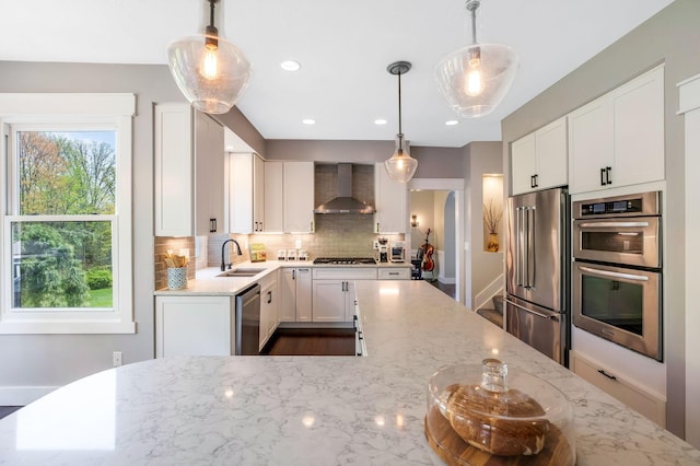 kitchen featuring decorative backsplash, light stone countertops, white cabinetry, wall chimney exhaust hood, and stainless steel appliances