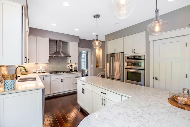 kitchen featuring backsplash, dark wood-style flooring, appliances with stainless steel finishes, a sink, and wall chimney exhaust hood