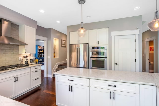 kitchen with wall chimney range hood, stainless steel appliances, white cabinetry, decorative backsplash, and dark wood-type flooring