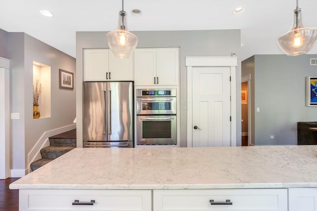 kitchen featuring appliances with stainless steel finishes, hanging light fixtures, light stone counters, and white cabinetry