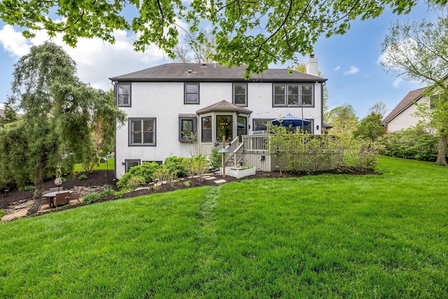 rear view of property featuring a lawn, stucco siding, a chimney, and a deck