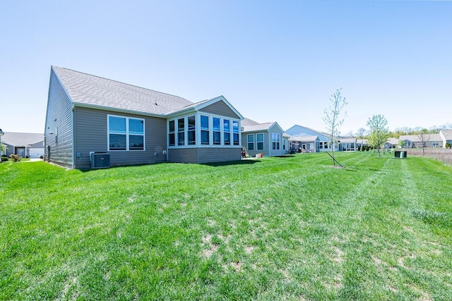 back of property featuring a lawn, a shingled roof, and central AC