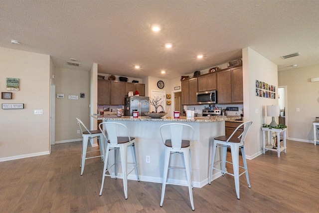 kitchen featuring appliances with stainless steel finishes, a kitchen breakfast bar, wood finished floors, and visible vents