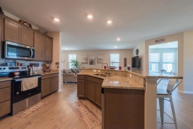 kitchen featuring a breakfast bar area, a sink, open floor plan, light wood-style floors, and stainless steel appliances