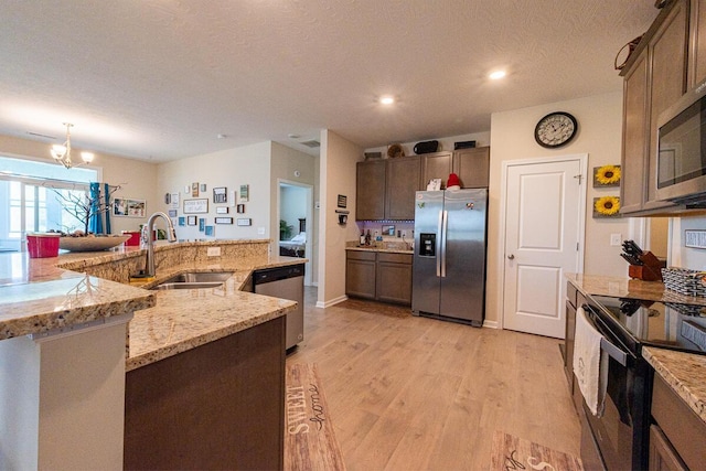 kitchen with a sink, light stone counters, an inviting chandelier, stainless steel appliances, and light wood-style flooring