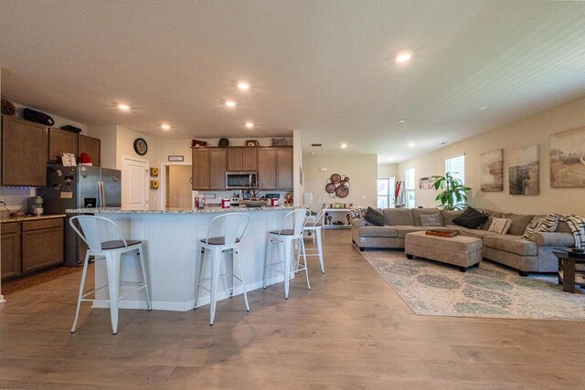 kitchen with appliances with stainless steel finishes, light wood finished floors, recessed lighting, open floor plan, and a kitchen bar