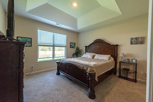 carpeted bedroom featuring baseboards, visible vents, and a raised ceiling