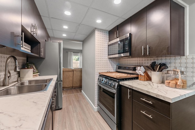 kitchen with decorative backsplash, appliances with stainless steel finishes, a sink, light wood finished floors, and recessed lighting