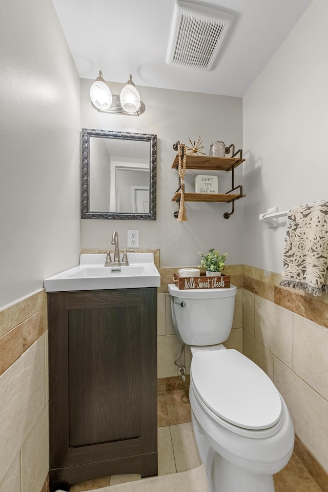 bathroom featuring tile walls, wainscoting, toilet, and visible vents