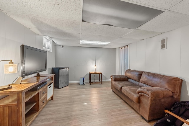 living room with light wood finished floors, a decorative wall, baseboards, a drop ceiling, and visible vents