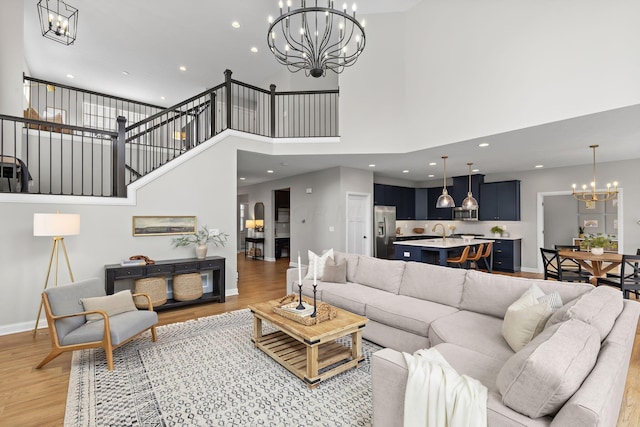living room featuring an inviting chandelier, baseboards, a high ceiling, and light wood-type flooring