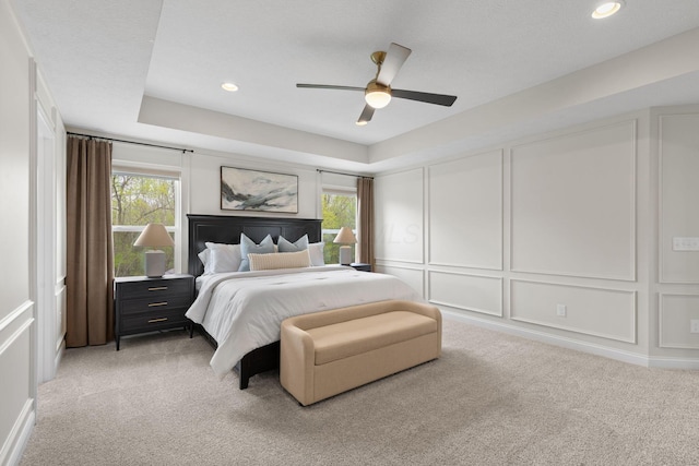 bedroom featuring multiple windows, a decorative wall, light carpet, and ceiling fan