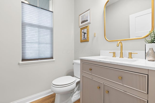 half bath with toilet, baseboards, wood finished floors, and vanity