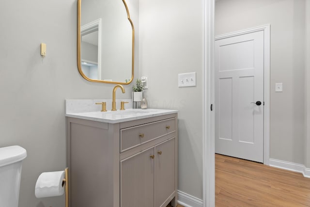 half bath with vanity, baseboards, wood finished floors, and toilet