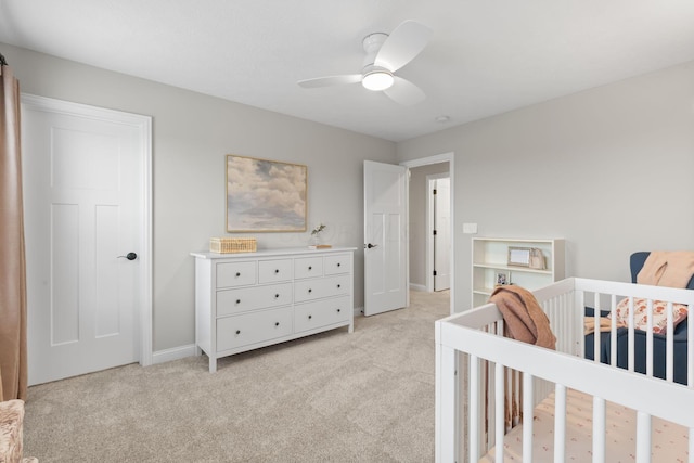 bedroom with a nursery area, baseboards, light carpet, and a ceiling fan