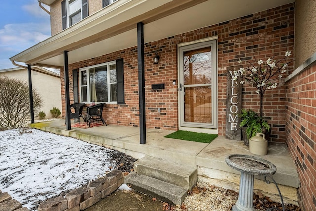 doorway to property with a porch and brick siding