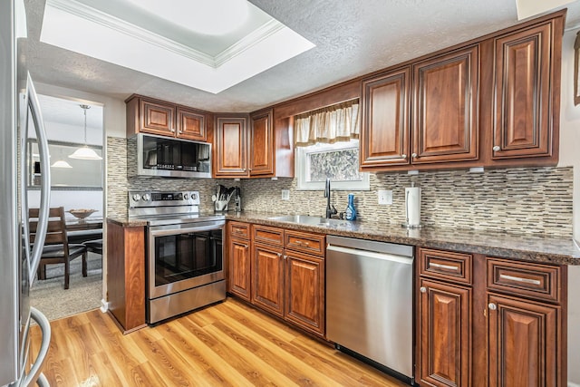kitchen with backsplash, brown cabinets, a sink, light wood finished floors, and stainless steel appliances