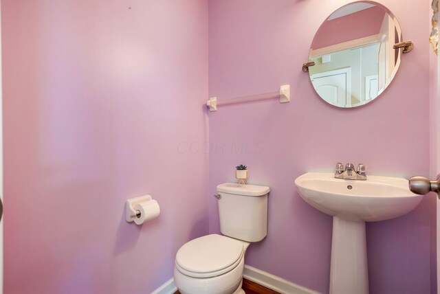 half bath with toilet, baseboards, and a sink