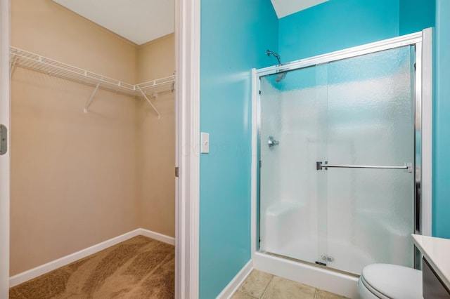bathroom with baseboards, a walk in closet, a stall shower, and toilet