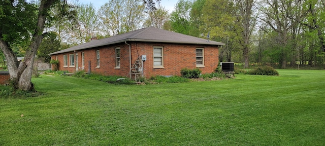 view of side of property with a yard, brick siding, central AC, and a chimney