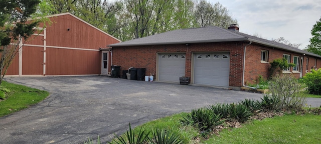 view of property exterior featuring a chimney, an attached garage, aphalt driveway, and brick siding