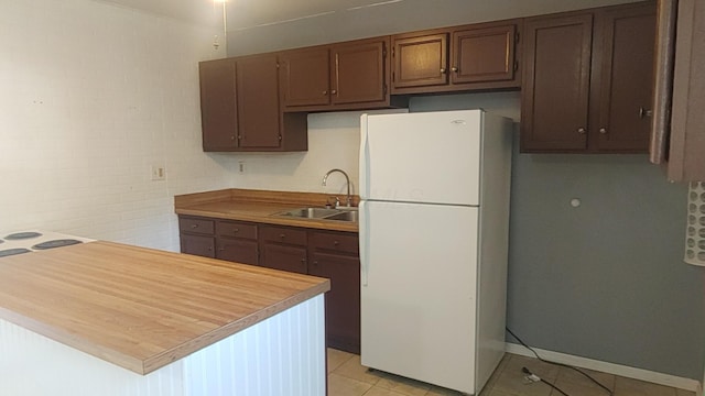 kitchen featuring a sink, baseboards, freestanding refrigerator, and light tile patterned flooring