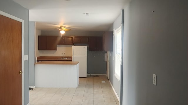 kitchen with a sink, freestanding refrigerator, a ceiling fan, and a peninsula