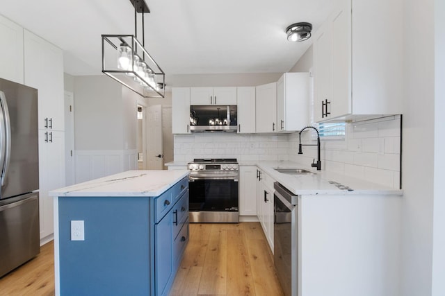kitchen with a kitchen island, a sink, light wood finished floors, appliances with stainless steel finishes, and blue cabinetry