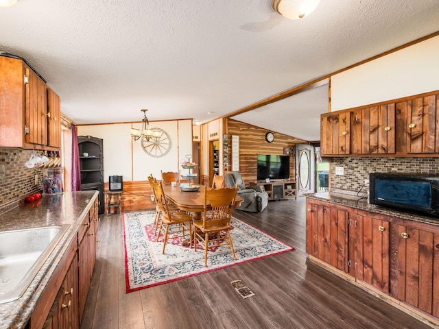 kitchen featuring wooden walls, dark countertops, a sink, brown cabinetry, and dark wood-style floors