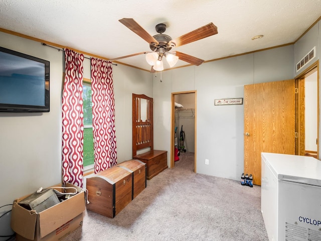 carpeted bedroom with fridge, visible vents, ornamental molding, and a walk in closet