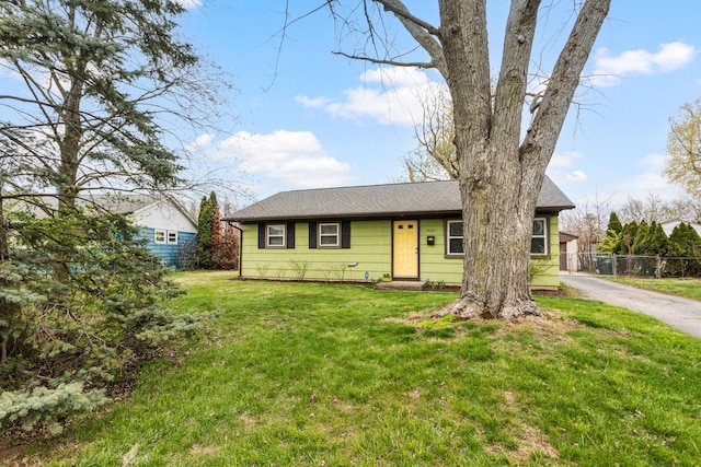 ranch-style home with fence, roof with shingles, and a front lawn