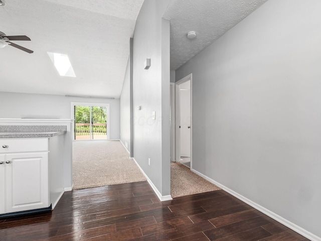hall with baseboards, a textured ceiling, dark wood-style flooring, and lofted ceiling with skylight