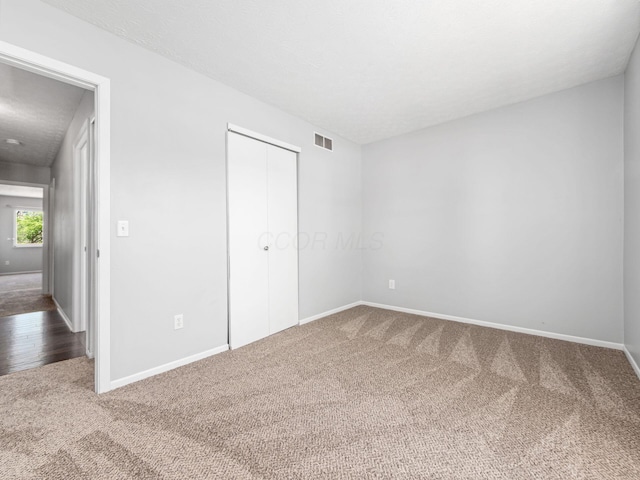 unfurnished bedroom featuring baseboards, carpet, a closet, and visible vents
