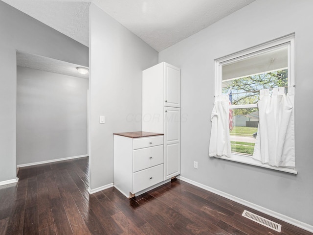 spare room featuring a textured ceiling, baseboards, visible vents, and dark wood finished floors