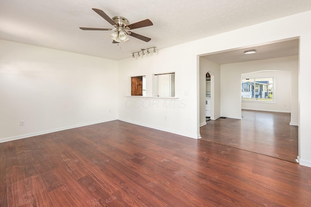 spare room with ceiling fan, dark wood-type flooring, track lighting, baseboards, and arched walkways