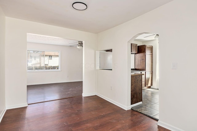 unfurnished room with baseboards, arched walkways, a ceiling fan, and dark wood-style flooring