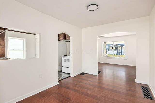 unfurnished room featuring baseboards, dark wood-style floors, and arched walkways