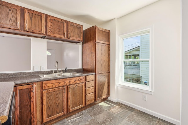 kitchen with dark countertops, brown cabinets, baseboards, and a sink