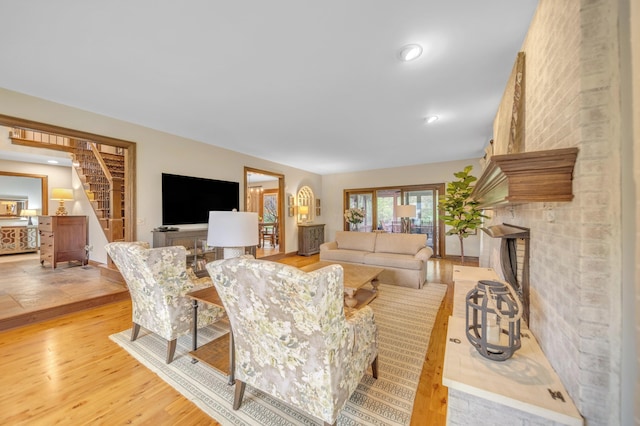 living area with a brick fireplace, baseboards, light wood finished floors, and stairs