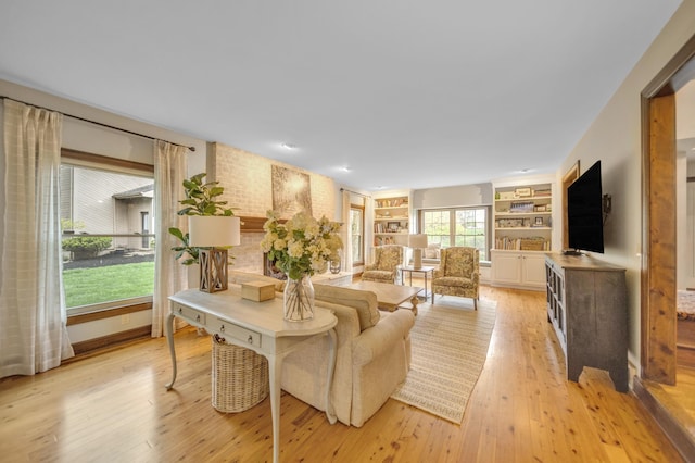 living area featuring baseboards, built in shelves, and light wood finished floors