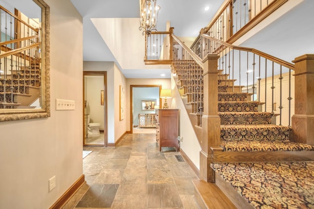 foyer featuring a chandelier, stone tile floors, stairs, visible vents, and baseboards