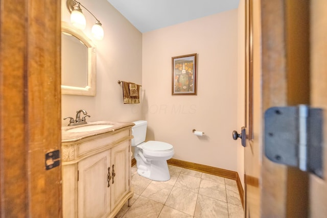 half bathroom with toilet, marble finish floor, vanity, and baseboards